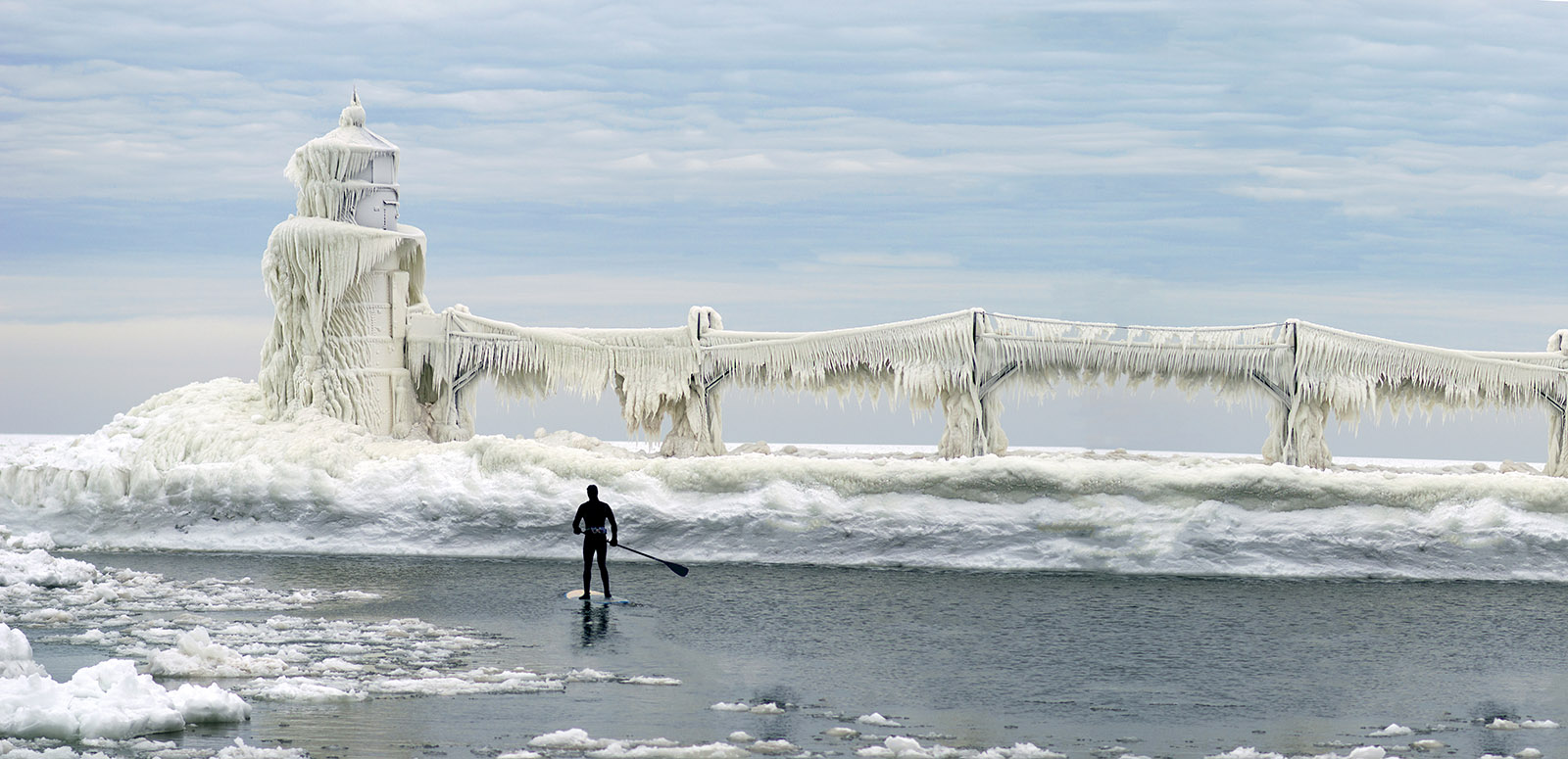 Paddleboarder in winter paddling past icy lighthouse