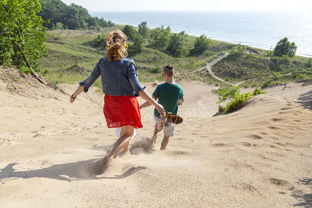 People running down a dune at Grand Mere State Park.