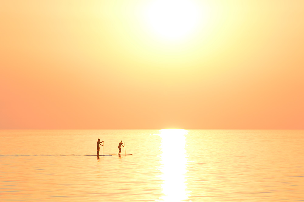 Two paddleboarders passing under the sunset on Lake Michigan.