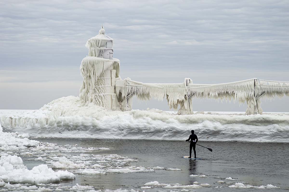 A paddleboard surfer braves the cold water and gets up close to the frozen lighthouse during their winter vacation